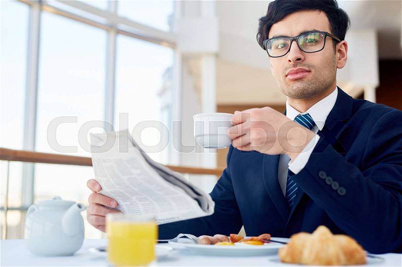 Confident leader with cup of tea and newspaper looking at camera, stock photo
