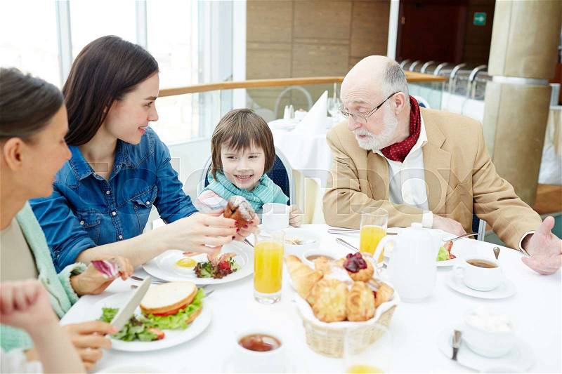 Grandparents, young woman and little boy sitting by dinner table, stock photo