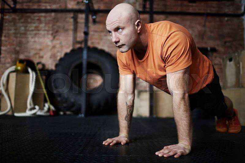 Handsome middle-aged sporty man wrapped up in intensive training: he flexing muscles while doing push-ups in gym, full-length portrait, stock photo
