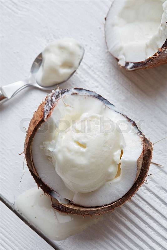 Ice cream in a half of coconut with a spoon On white wooden background, stock photo