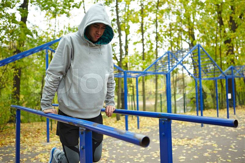 Young sportsman in hoodie doing street workout exercise, legs bent at knee, full-length portrait, stock photo