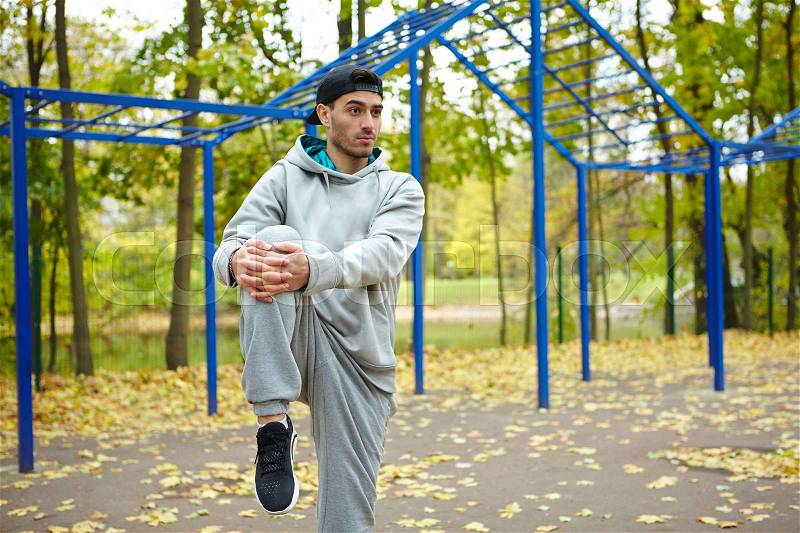 Sporty young man doing warm-up exercises while enjoying picturesque view of autumn park, stock photo