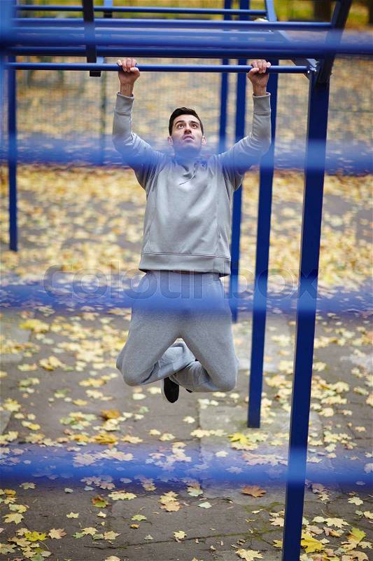 Having training in street workout park: young sporty man doing pull-ups on bar, full-length portrait, stock photo
