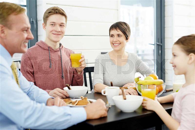 Joyful family members gathered together in dining room, enjoying tasty breakfast and chatting animatedly, waist-up portrait, stock photo