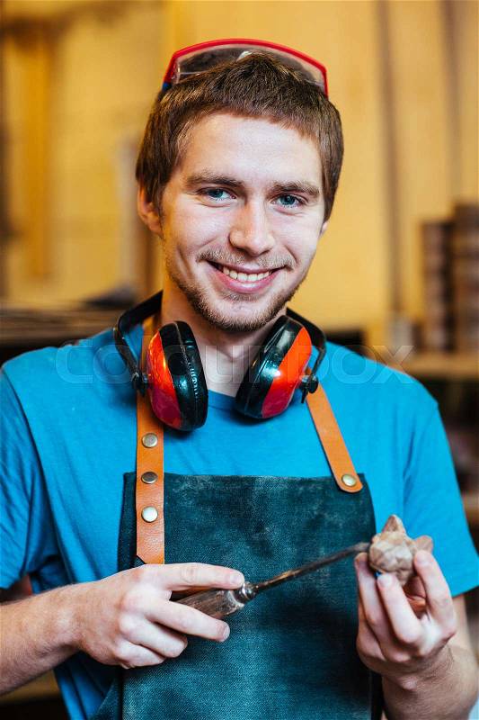 Portrait of young carpenter smiling cheerfully looking at camera and making wooden toy, stock photo