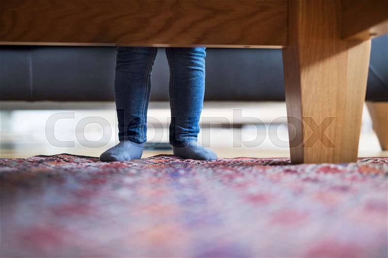 Little girls legs at home standing behind sofa, stock photo