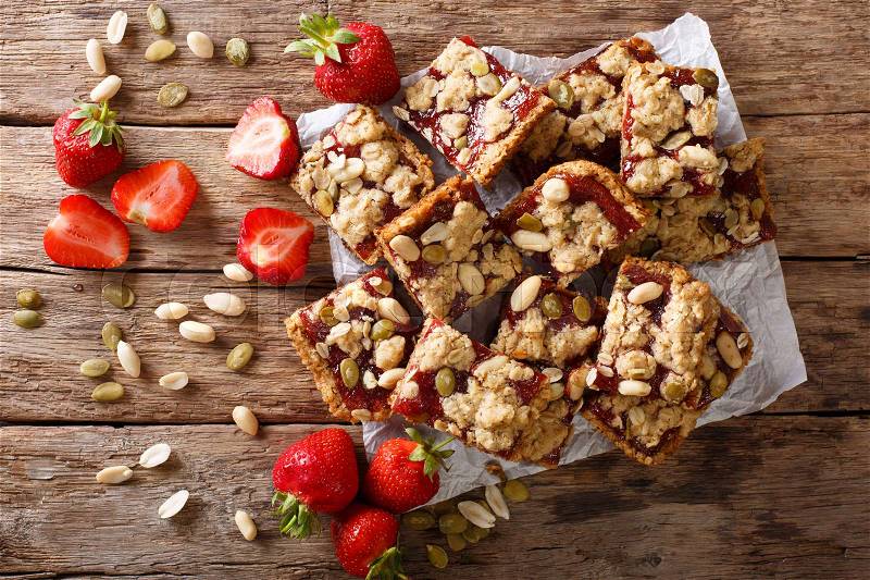 Homemade strawberry bars with oatmeal, peanuts and pumpkin seeds close-up on the table. horizontal view from above , stock photo
