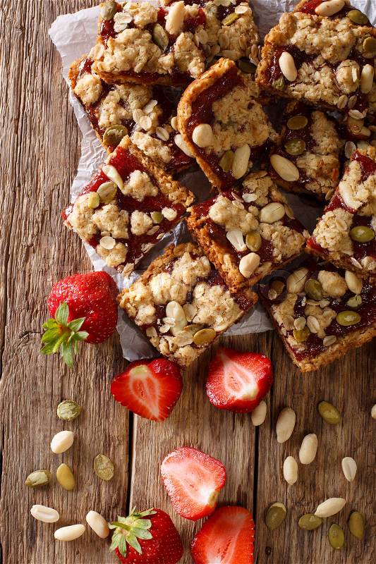 Oat bars with strawberries, seeds and nuts close-up on the table. Vertical view from above , stock photo