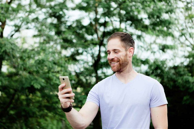 Casual guy in a park taking a photo with his mobile, stock photo