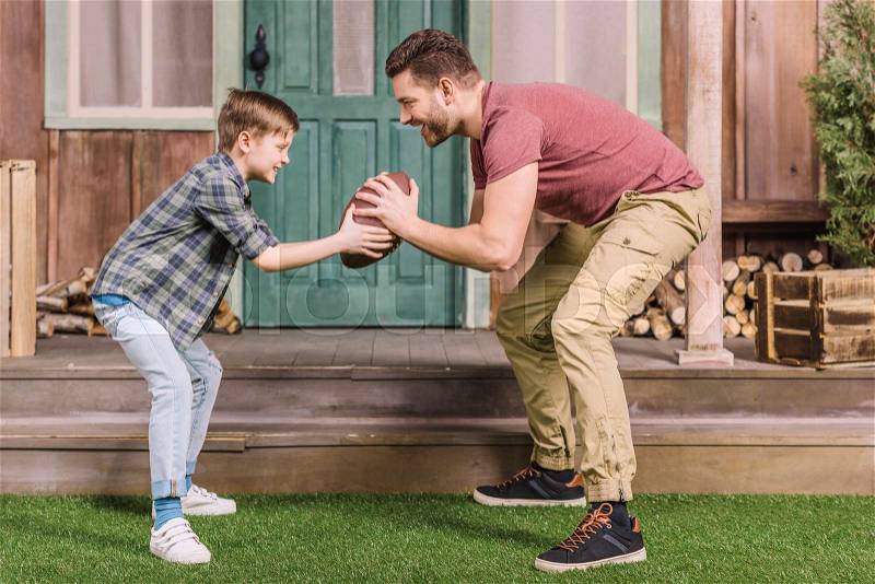 Father with little son playing american football with ball at backyard, dad and son playing, stock photo