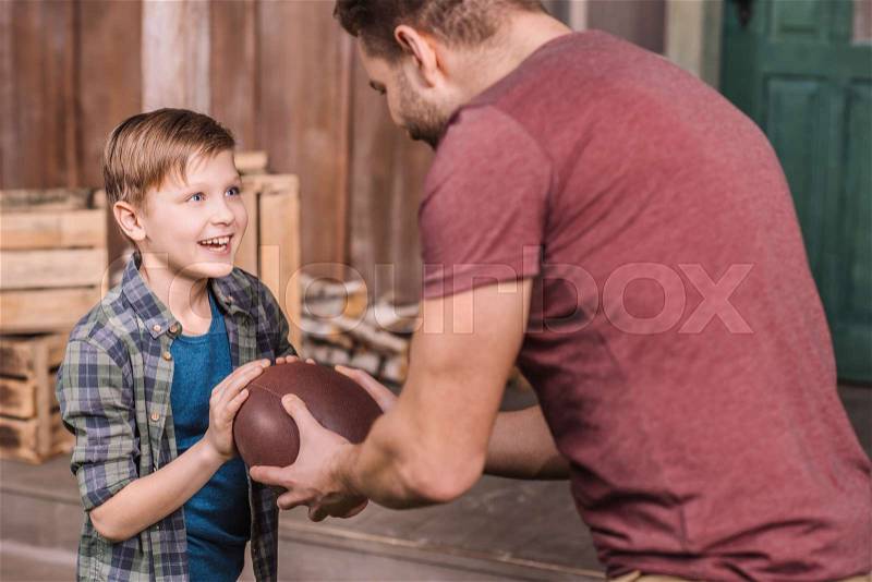 Father with little son playing american football with ball at backyard, dad and son playing, stock photo