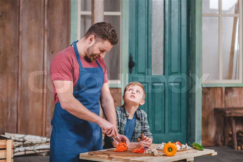 Smiling father and son cutting fresh vegetables at backyard, dad and son cooking concept, stock photo