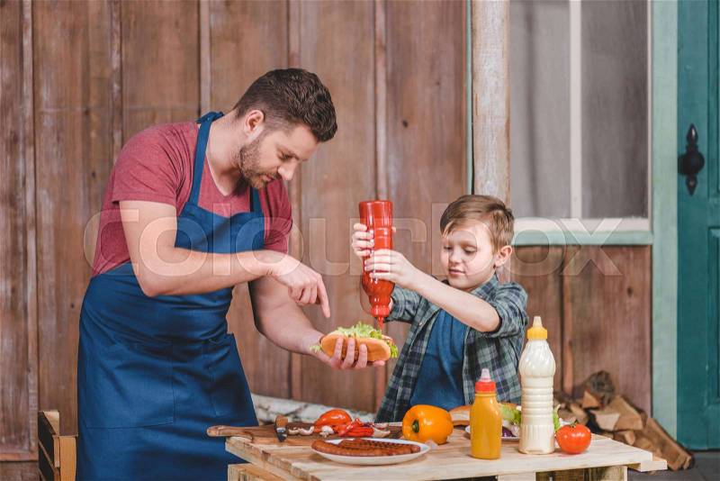 Smiling little boy with father cooking hot dog at backyard, dad and son cooking concept, stock photo