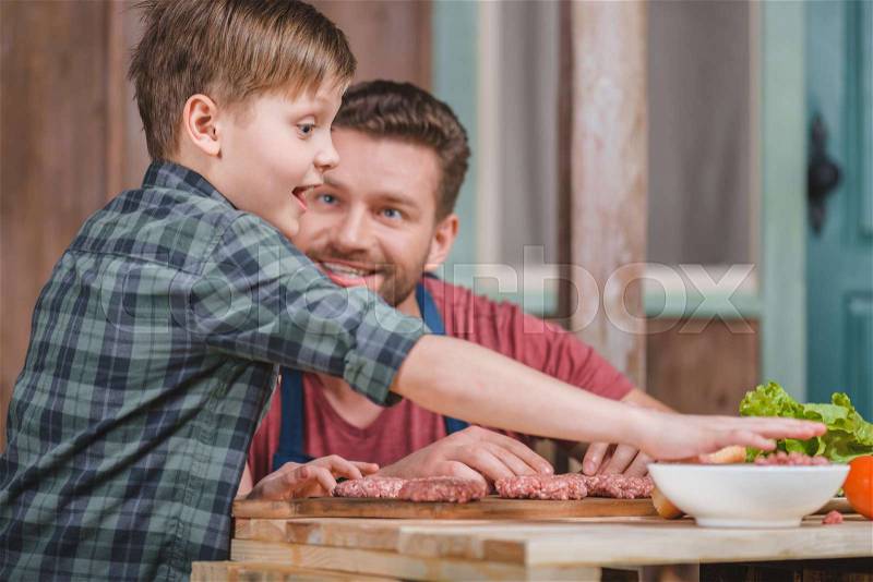 Happy father and son cooking meat patties together, dad and son cooking concept, stock photo