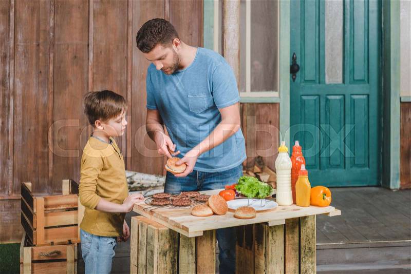 Side view of dad and son cooking meat burgers together, stock photo