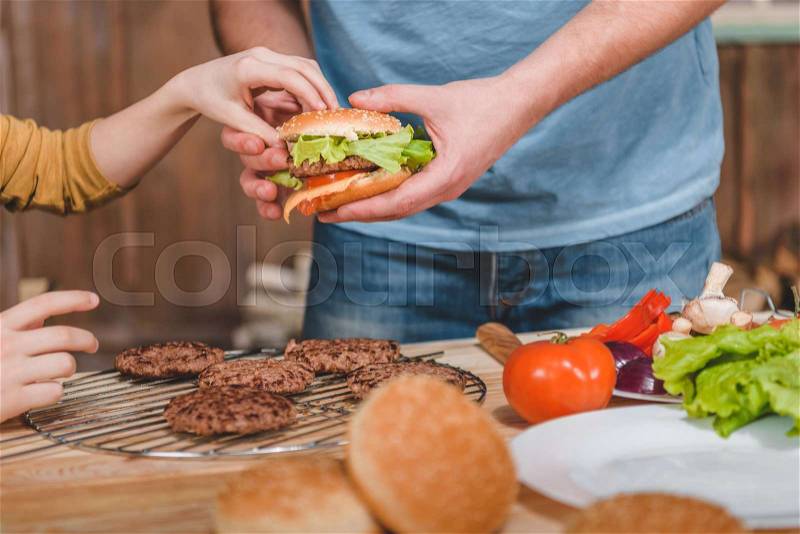 Partial view of dad and son cooking meat burgers together, stock photo