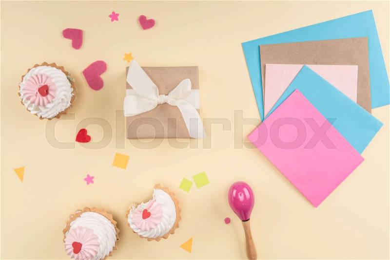 Top view of happy birthday lettering, cakes, envelopes and gift box on beige, birthday party concept , stock photo