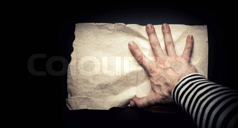 Strong sailor hand catching empty old crumpled paper sheet on black background, pirate map concept, stock photo
