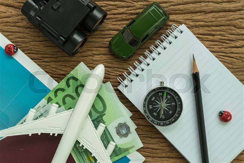 Travel planning concept with airplane euro banknotes, passport, compass, binoculars, pencil, paper note and miniature car on wood table, stock photo