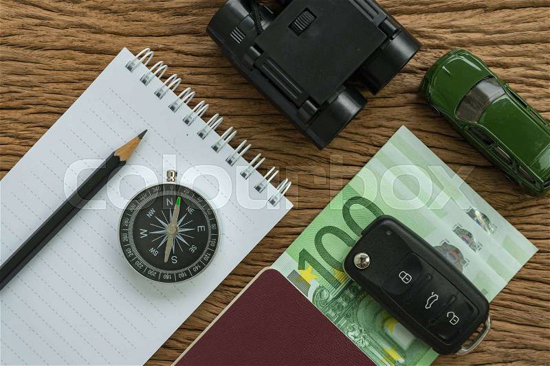 Travel planning road trip concept with euro banknotes, passport, compass, binoculars, pencil, paper note, car key and miniature car on wood table, stock photo