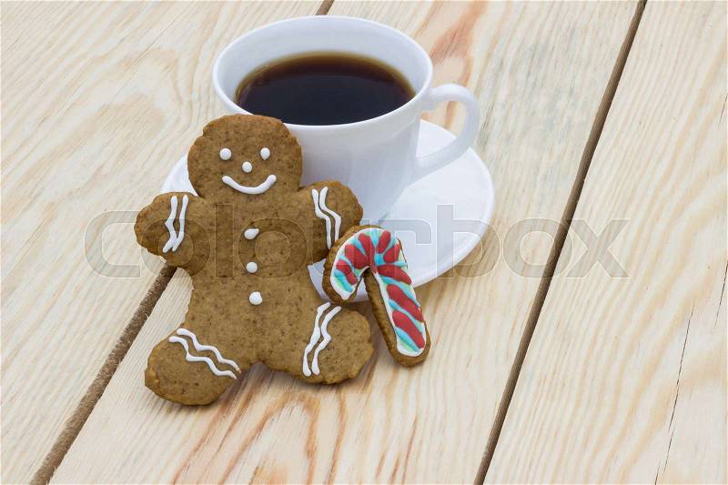 Homemade gingerbread cookie man and cup of coffee on wooden table, stock photo