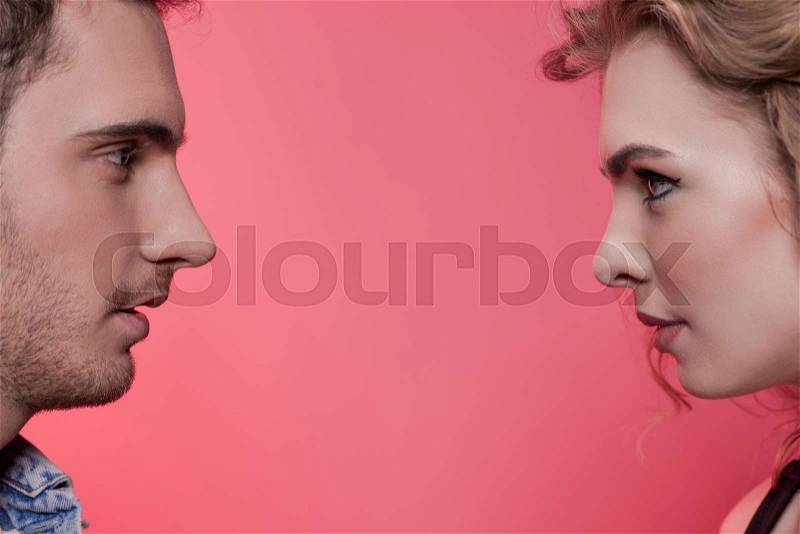 Side view of stylish young couple in love looking at each other isolated on pink, stock photo