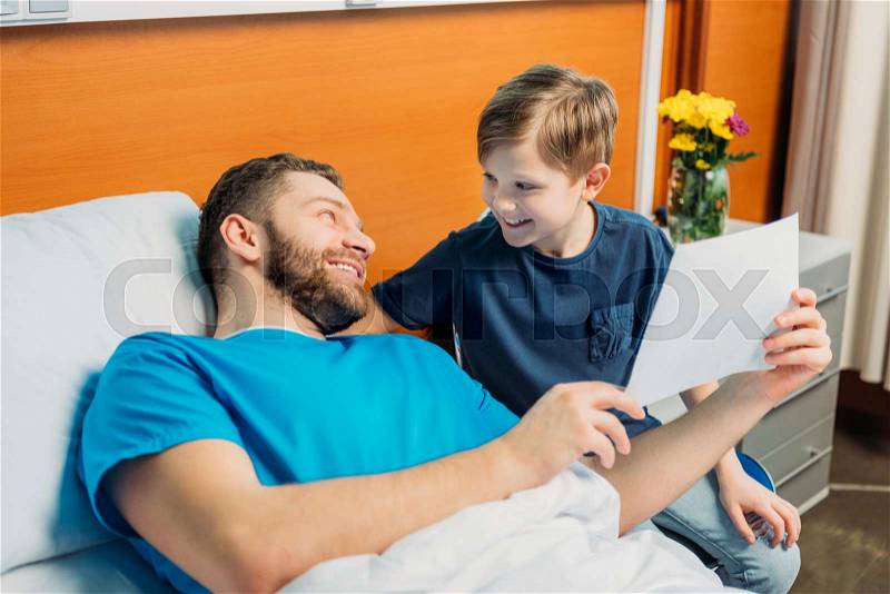 Little son showing sick father his drawings at ward, hospital patient care, stock photo