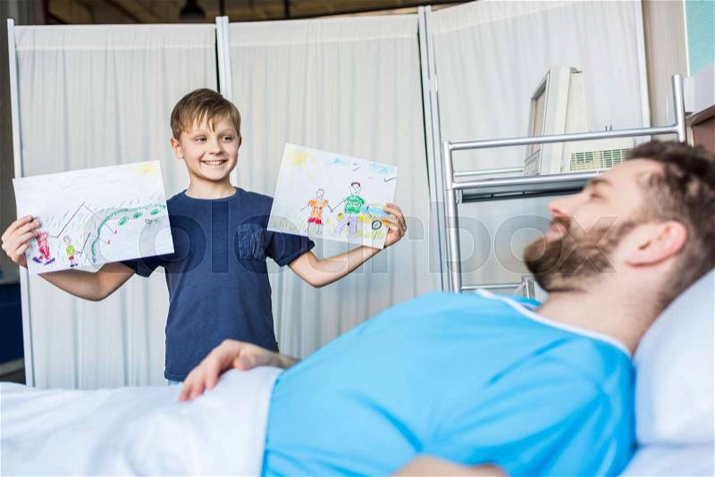 Little son showing sick father his drawings at ward, dad and son, stock photo