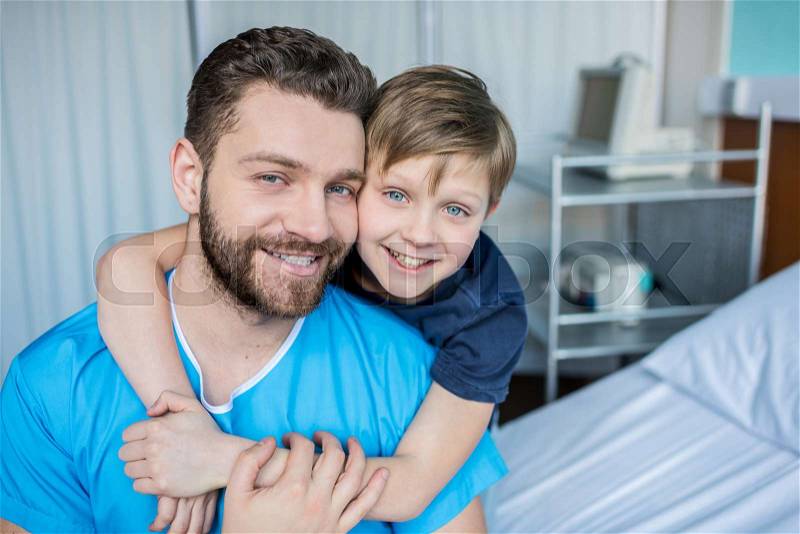 Father and son hugging while sitting on hospital bed, dad and son in hospital , stock photo