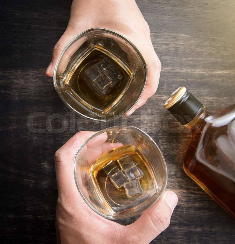 Glass of whiskey in hand and whiskey bottle on wooden table,top view, stock photo