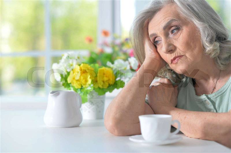 Beautiful old woman is sad at the table, stock photo