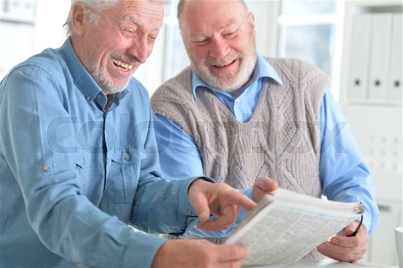 Old men reading a newspaper at a table, stock photo
