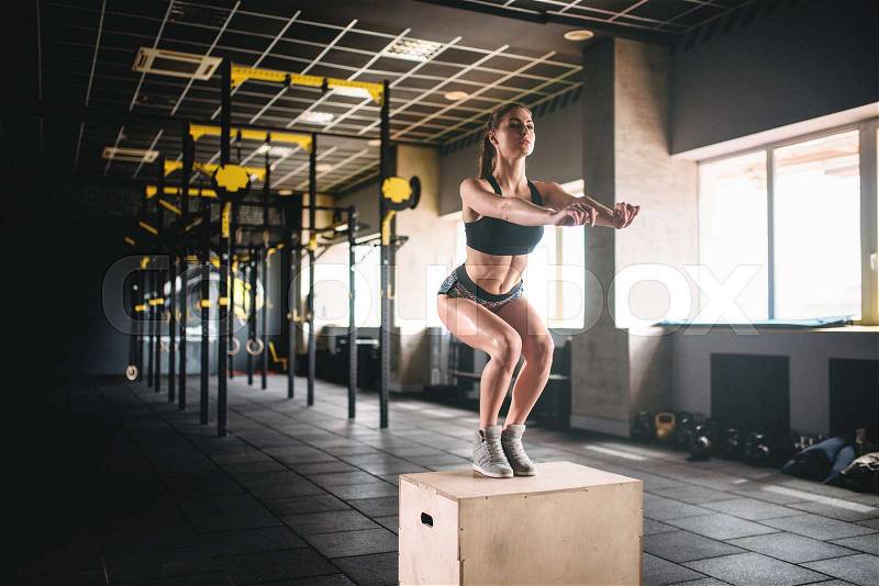 Young woman doing box jump exercise in fitness club. Attractive female athlete workout in gym, stock photo