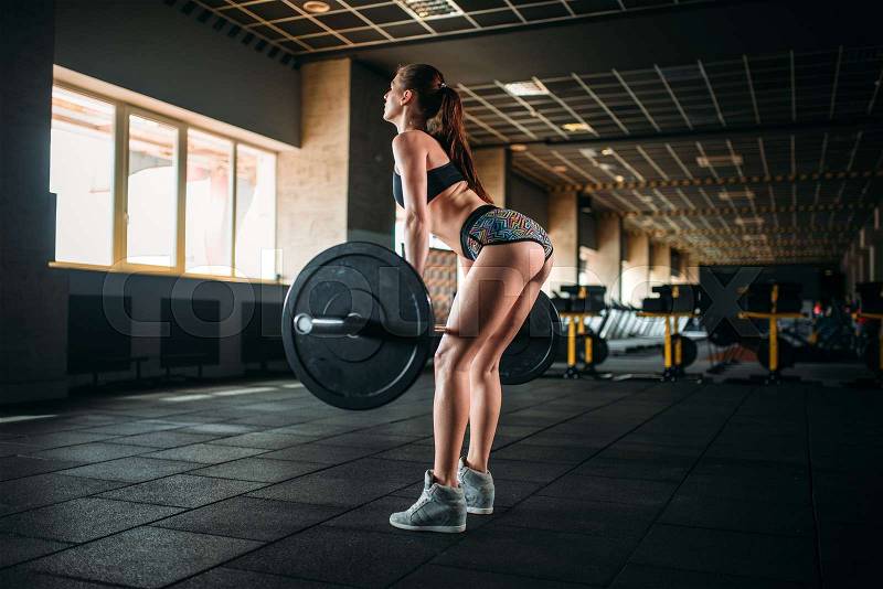 Muscular female athlete training with barbell in sport gym. Woman exercise with weight in fitness club, stock photo