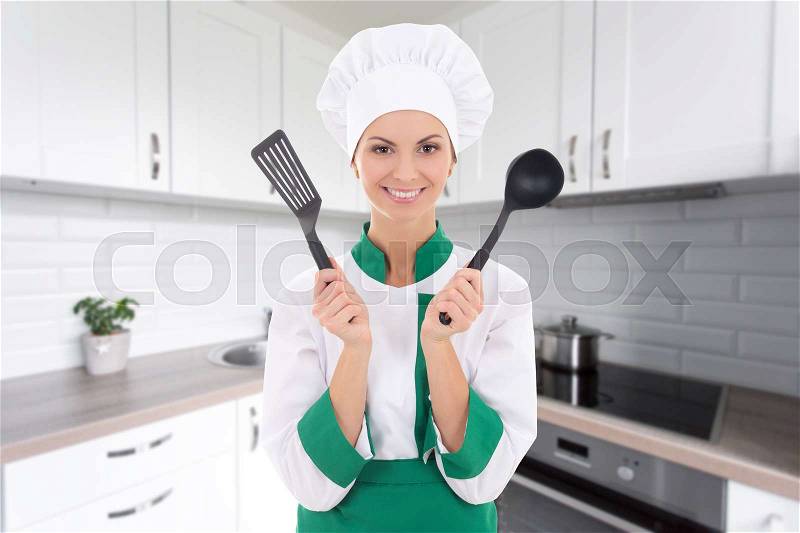 Young cheerful chef woman in uniform with tools in modern kitchen, stock photo