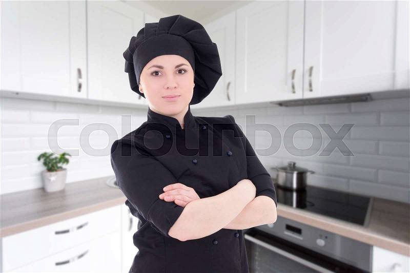 Young beautiful chef woman in black uniform posing in modern kitchen, stock photo
