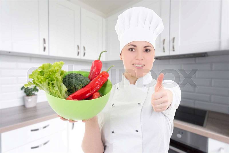 Young cook woman in uniform with vegetarian food thumbs up in modern kitchen, stock photo