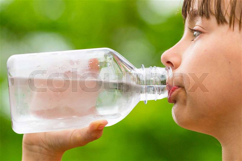 Closeup of young child drinking pure tap water from transparent plastic drinking bottle while outdoors on a hot summer day, stock photo