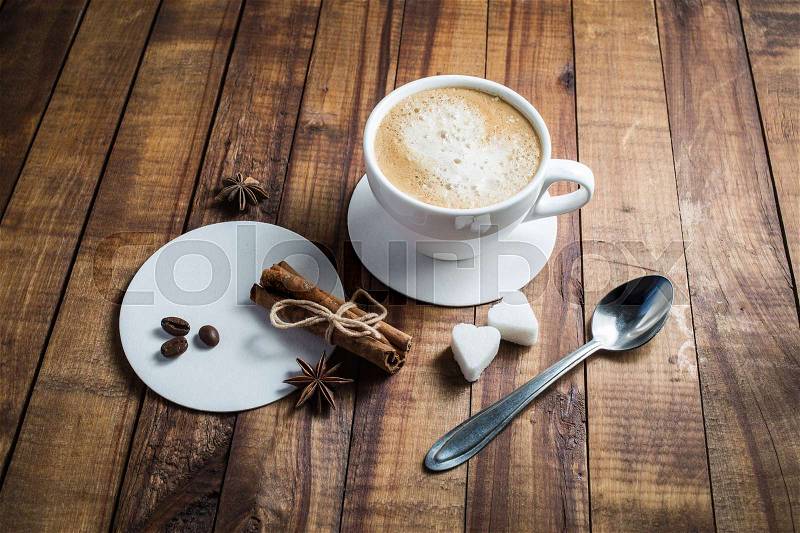 Coffee with spices. Coffee cup, cinnamon sticks, coffee beans, anise, sugar, spoon and coasters on vintage wooden kitchen table background, stock photo