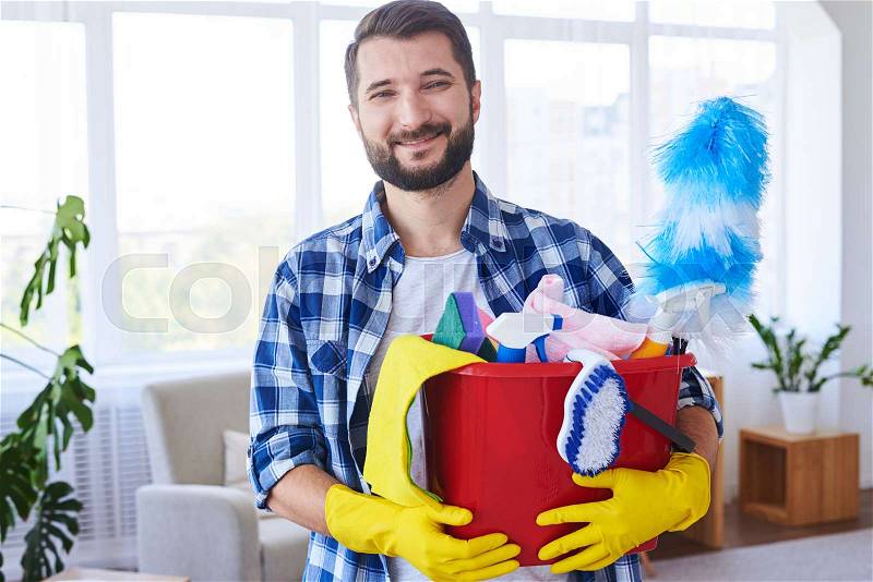 Close-up of handsome man holding nice set for cleaning in bright room, stock photo