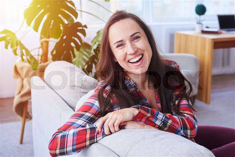 Mid shot of brunet laughing and having rest sitting on stylish sofa, stock photo