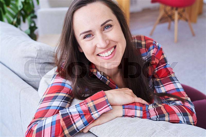 Close-up of attractive brunet smiling and having rest sitting on stylish sofa, stock photo