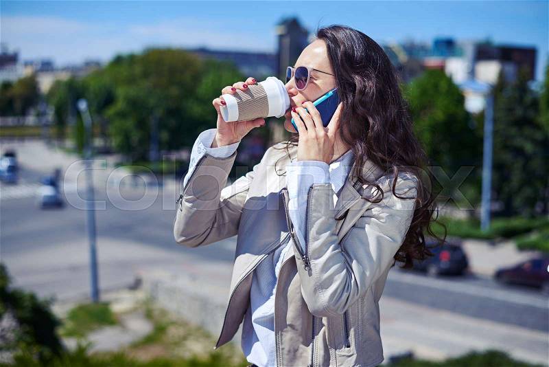Mid shot of gorgeous lady talking on phone while drinking coffee on top of building, stock photo