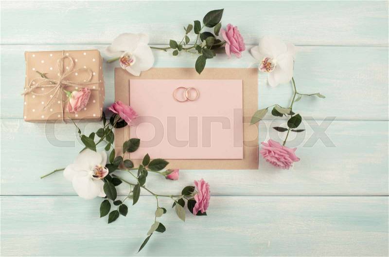 Pink roses, orchid, bridal rings and gift box with emty paper for wedding invitations on background of shabby wooden planks. Top view. Flat design. Copy space, stock photo