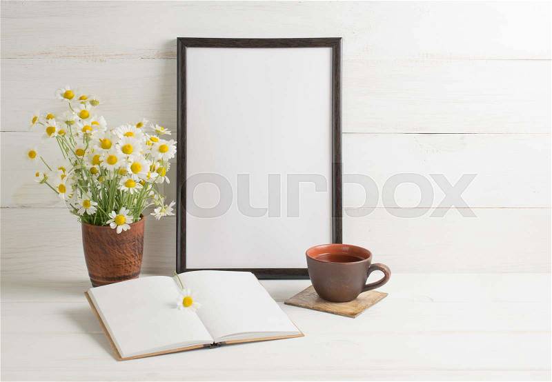 Daisy bouquet with motivational frame, open notebook and cup tea on background of white wooden planks in scandinavian style. Home interior, stock photo