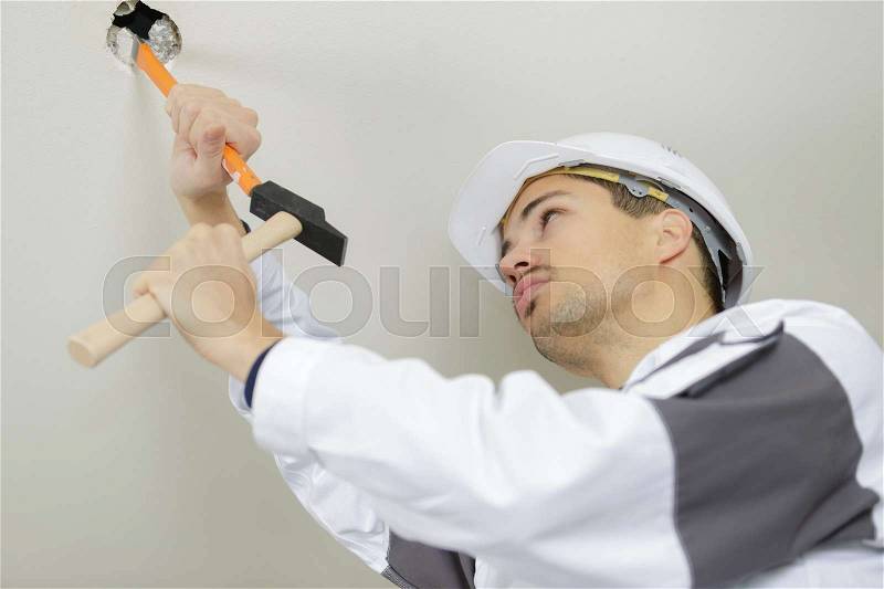 The worker scrapes the old paint on the ceiling, stock photo