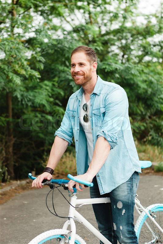 Handsome man with denim clothes enjoying with his bike in the park, stock photo