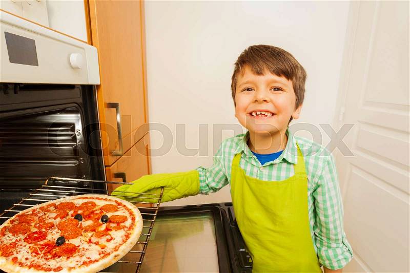 Portrait of cute little chef, six years old boy, baking tasty pizza in the oven, stock photo