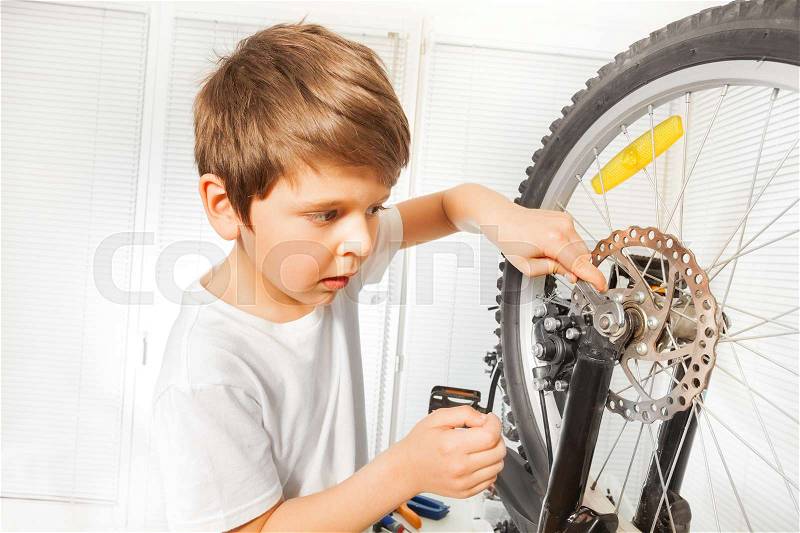 Close-up portrait of Caucasian boy repairing his bicycle, drawing up a bolt tight with spanner at garage, stock photo