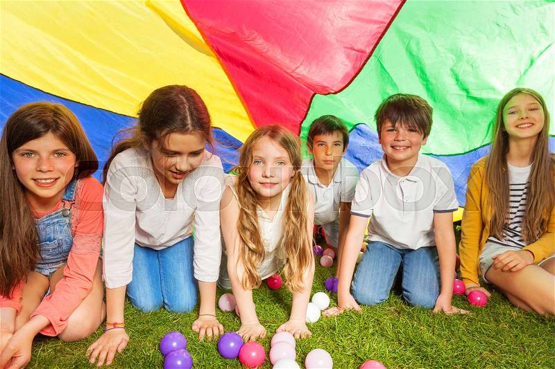 Portrait of happy kids hiding under canopy made of colorful parachute outdoors in summer, stock photo